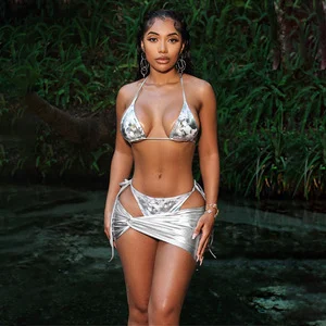 woman in a silver bikini and wrap, posing confidently in a lush outdoor setting