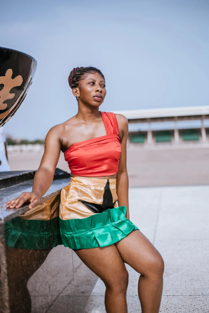 woman in a red top and colorful skirt poses confidently by a stone surface against a clear sky